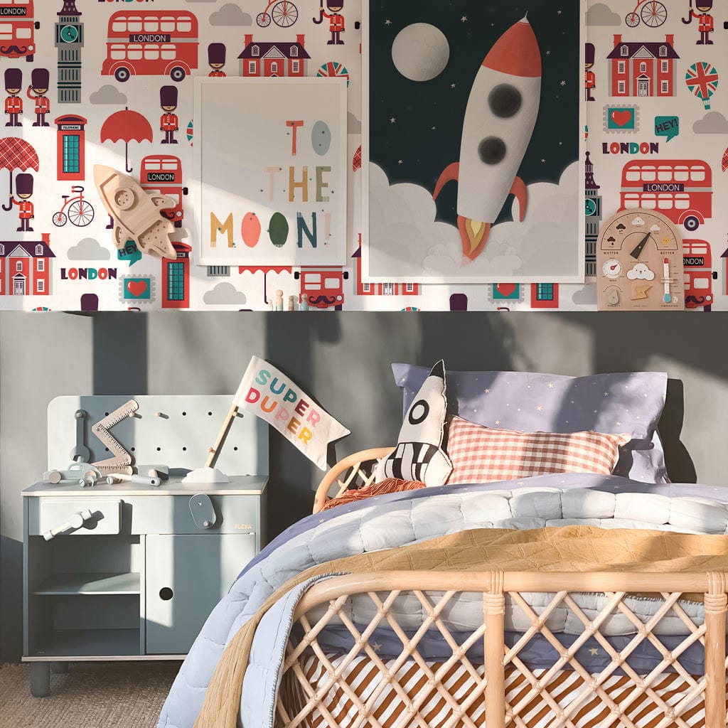 Children's room with London-themed wallpaper, wicker bed, blue side table, and rocket-themed decor.