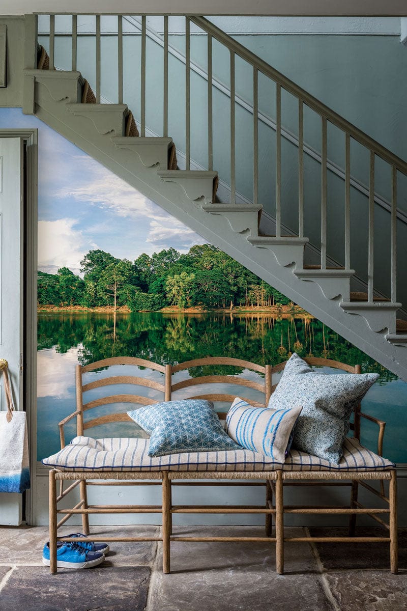 Staircase area with Serene Lakeside Forest Landscape Mural Wallpaper, wooden bench, stone flooring, decorative cushions.