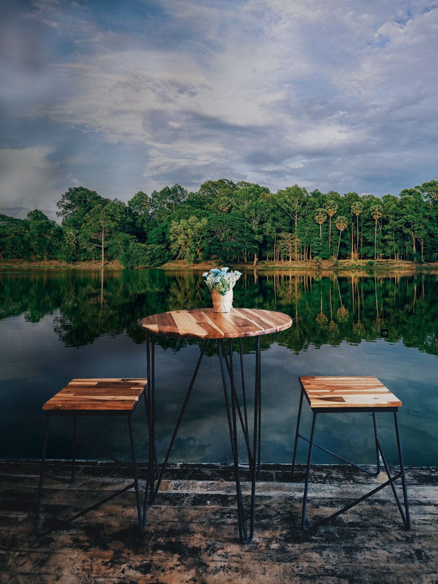 Small wooden bistro set beside Serene Lakeside Forest Mural Wallpaper, enhancing natural decor harmony.