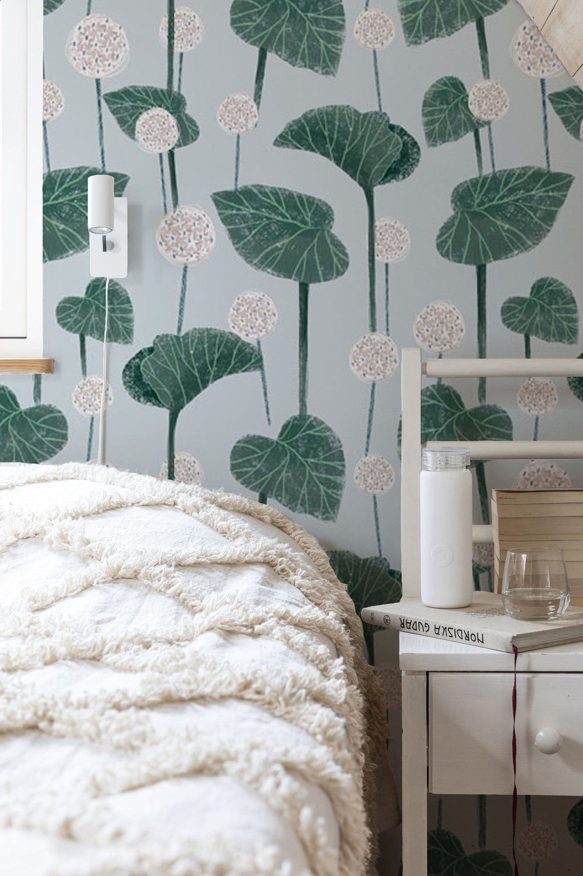 Elegant green botanical wallpaper in bedroom with white bed, textured throw, and light wooden furniture.