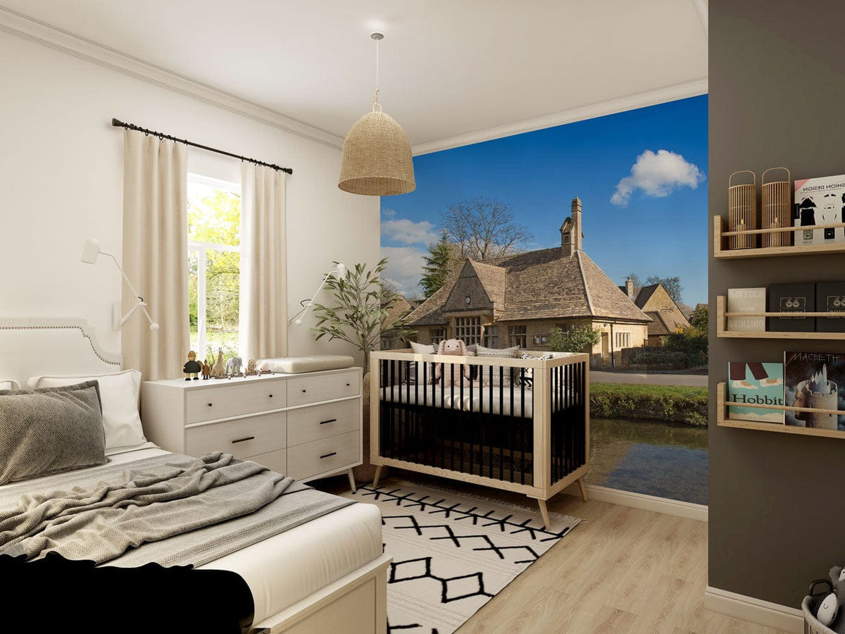 Charming Cotswold mural wallpaper in baby's room, warm stone hues, light wood flooring, white walls.