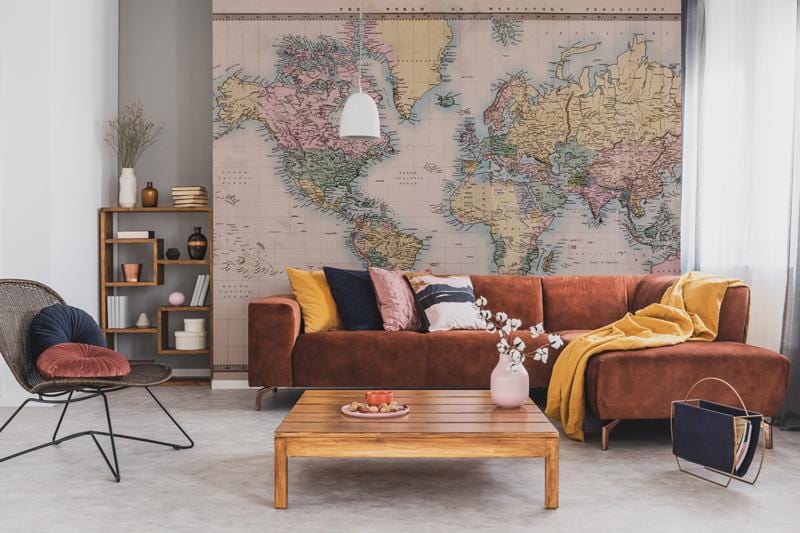 Vintage sepia world map wallpaper with brown velvet sofa, wooden coffee table, and modern shelving.