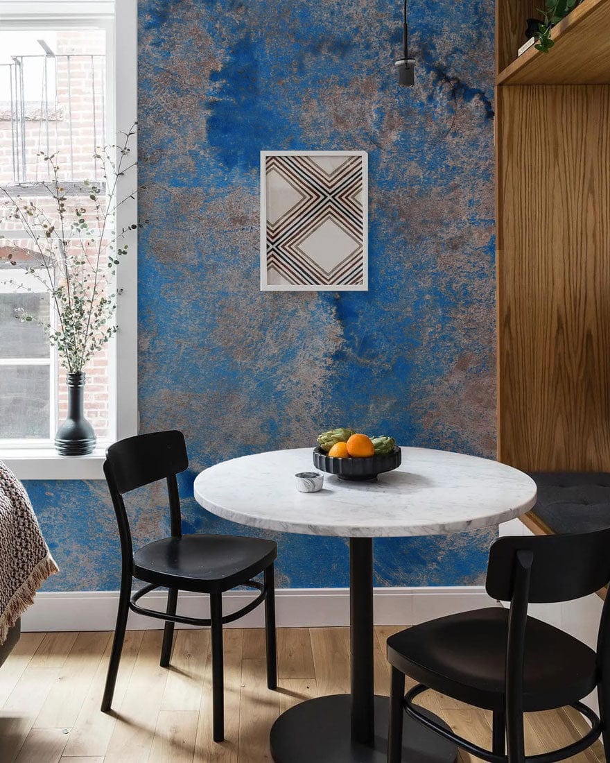 Abstract blue earth tones mural wallpaper in dining room with black chairs, marble table, wooden flooring.