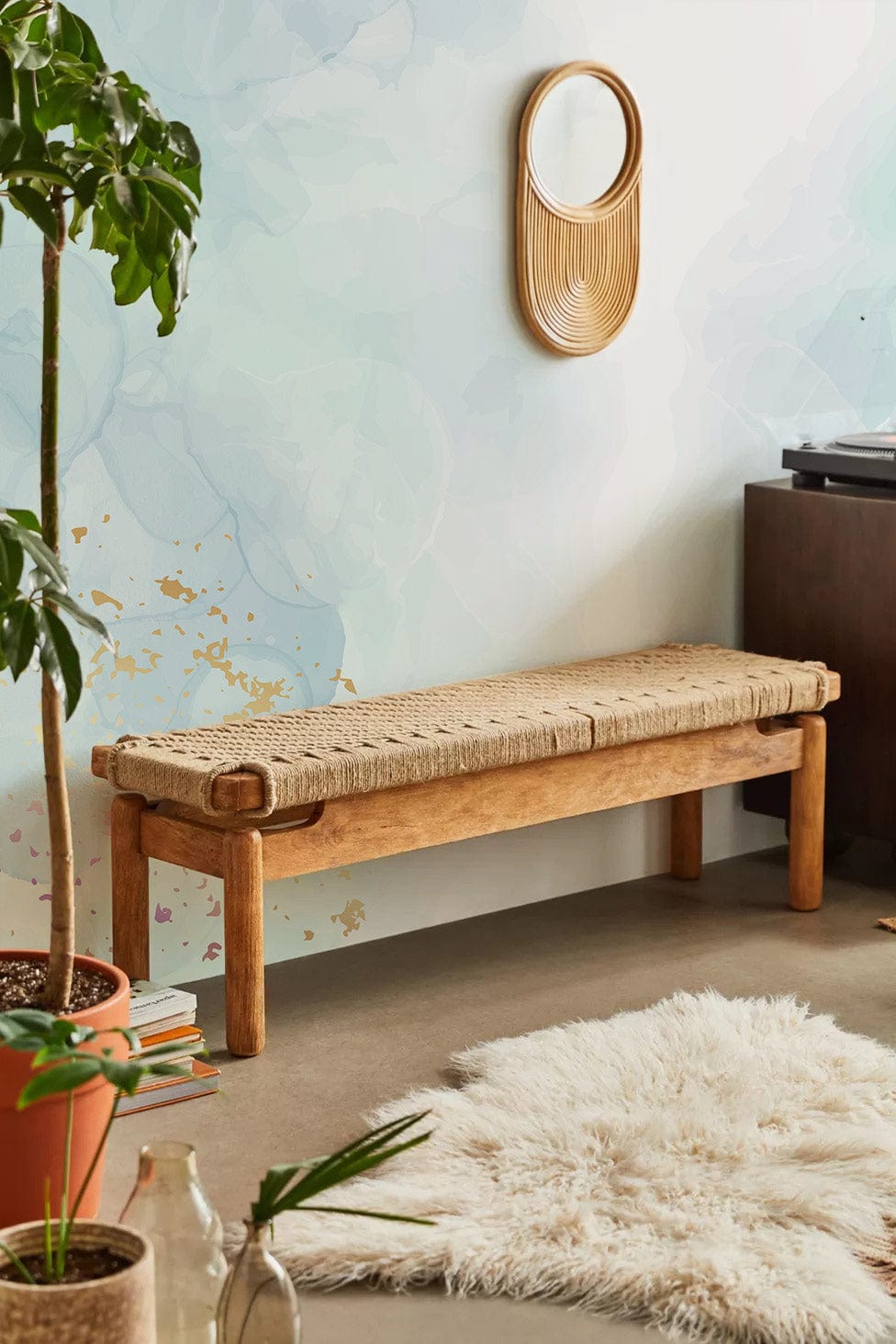 Tranquil watercolour mural with gold accents, wicker bench, wool rug, abstract wall, and wooden mirror.