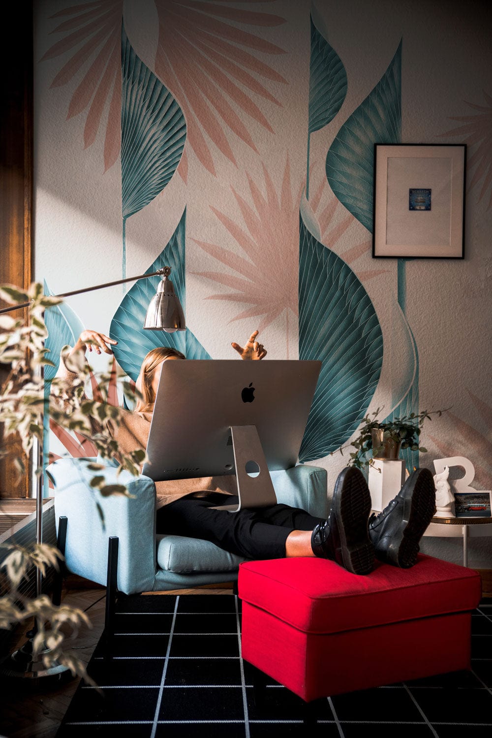 Tropical blue and coral leaf wallpaper with modern design; cosy living room, blue chair, red ottoman.