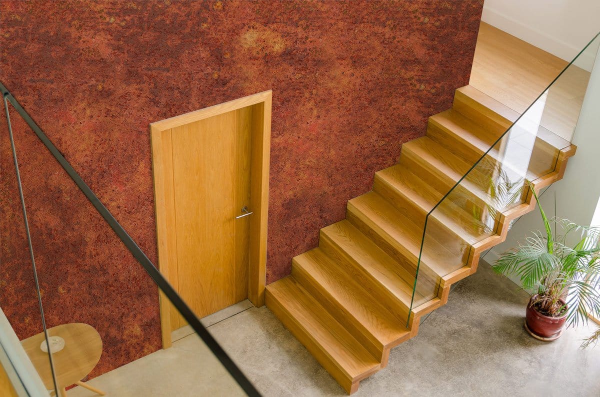 Rustic burnt orange textured mural wallpaper, modern staircase, wooden door, sleek glass railing, hallway setting.