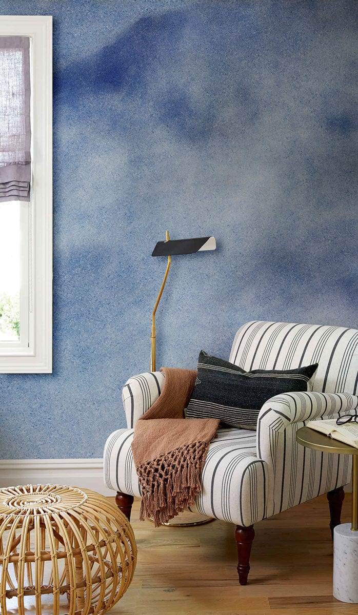 Serene Sky Blue Watercolour Wallpaper, striped armchair, modern lamp, wooden flooring in cosy living room.