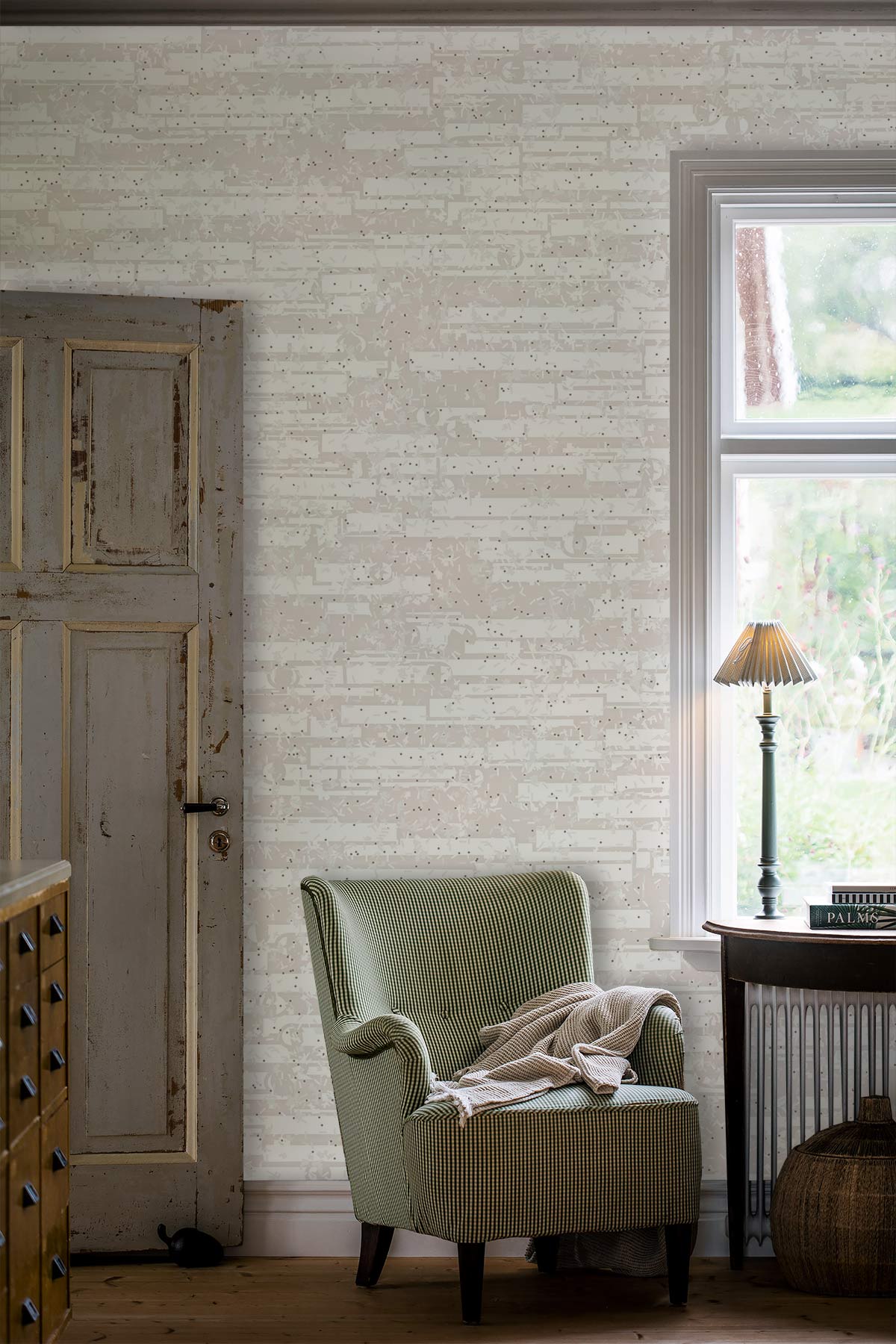 Neutral brick pattern wallpaper with green armchair, rustic door, wood flooring, and side table lamp.
