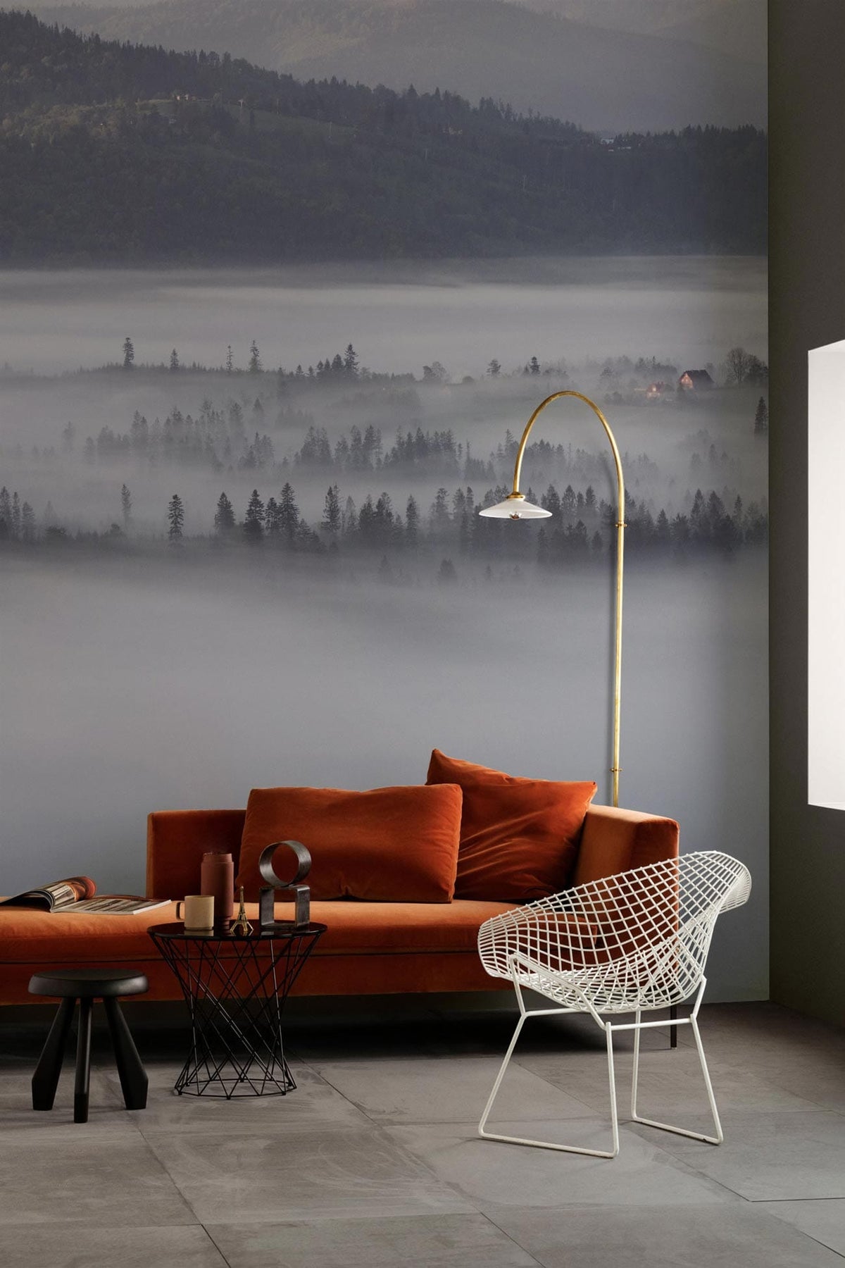 Misty Mountain Forest Landscape Mural Wallpaper in grey-blue, orange sofa, modern chair, grey floor tiles.