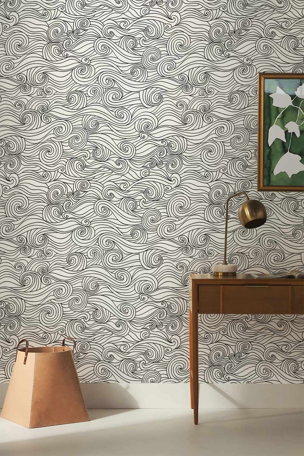 Monochrome swirling waves wallpaper, modern interior style, with wooden desk, wall art, and lamp.