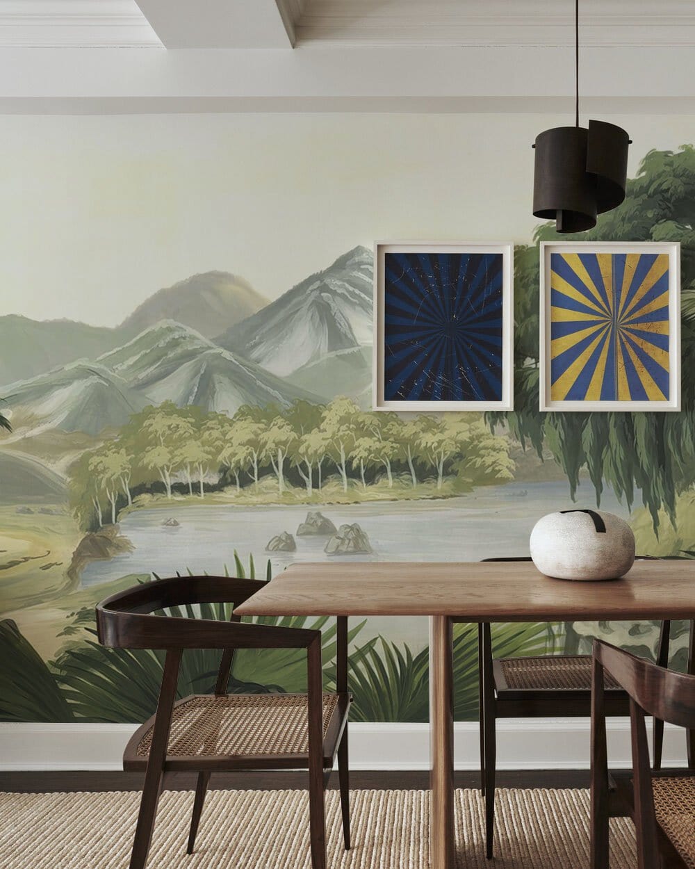 Tranquil mountain landscape mural wallpaper in dining room with wooden table, wicker chairs, and artwork.