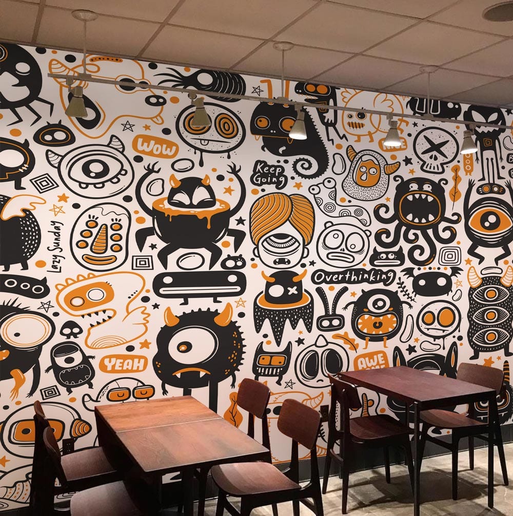Playful Doodle Monster mural wallpaper pattern in black and orange, café setting with wooden tables and chairs.