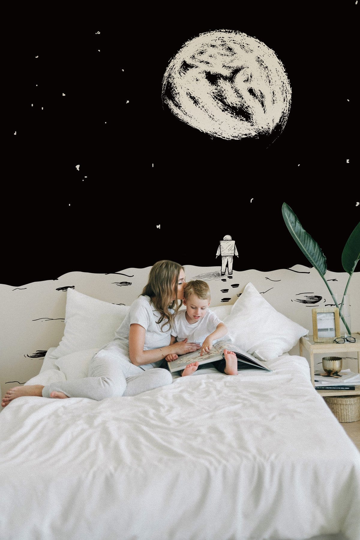 Monochrome astronaut moon landing wall mural in bedroom, with white bedding and light wood side table.
