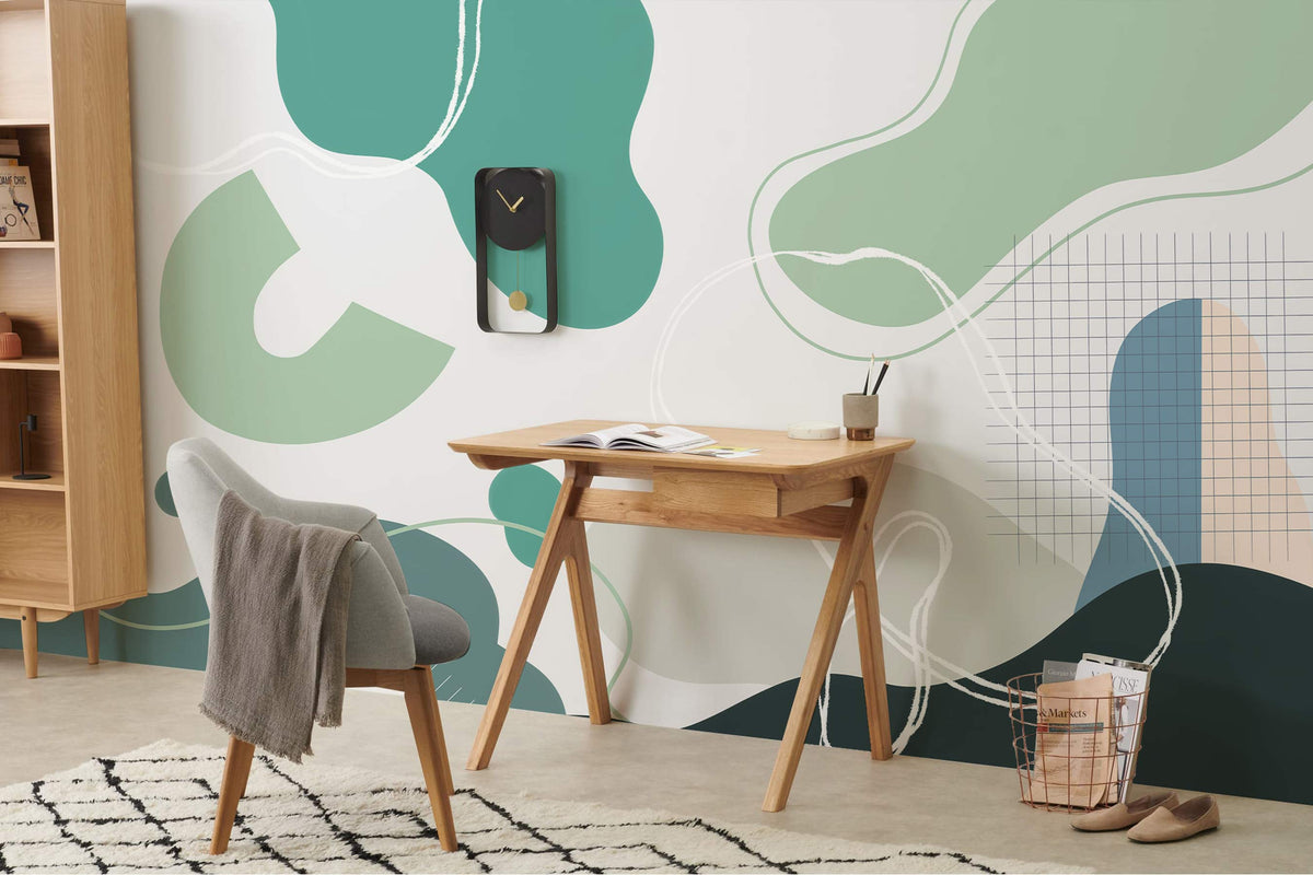 Abstract green and teal geometric mural wallpaper in modern study with wood desk, grey chair, rug.