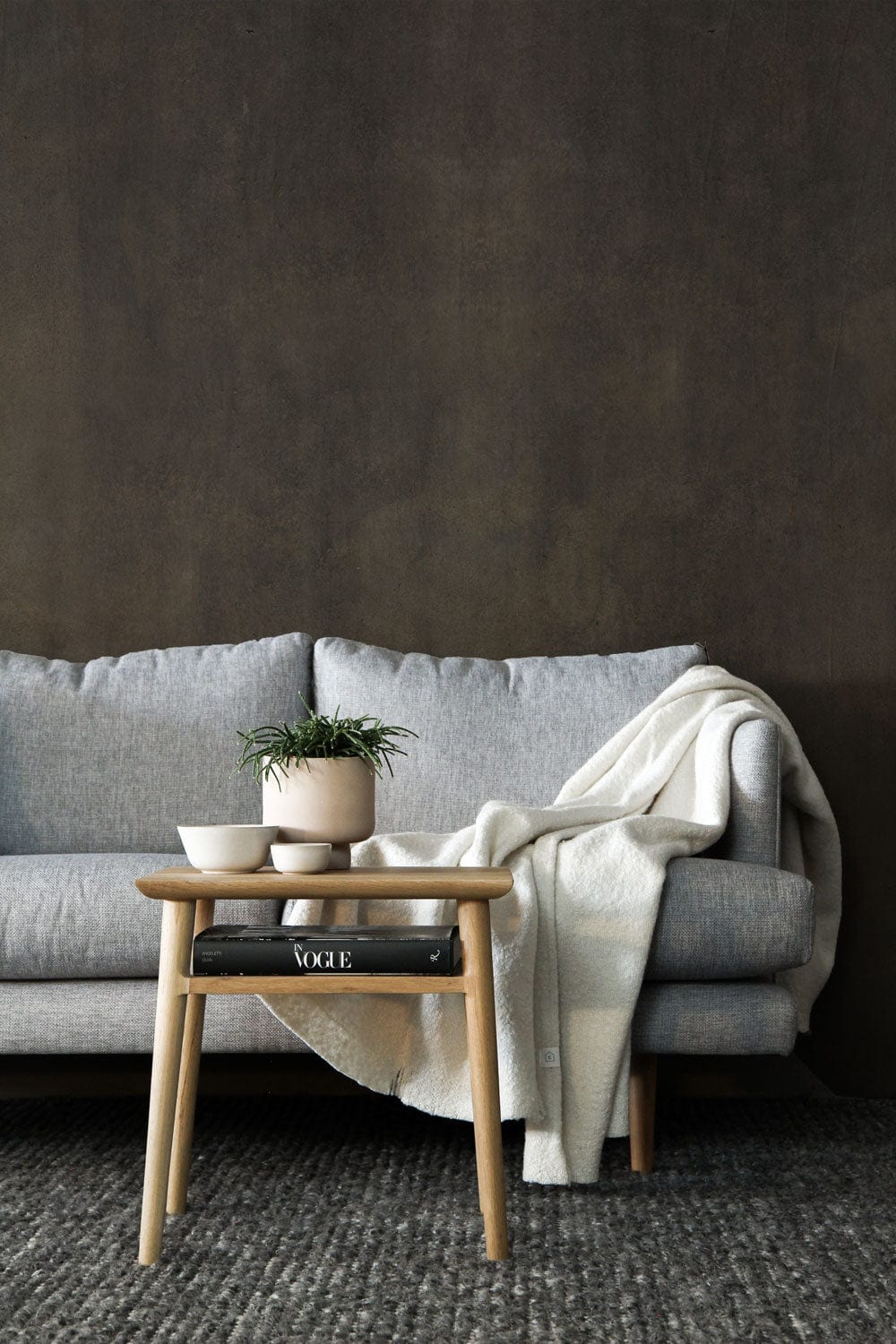 Vintage rustic charcoal wallpaper with grey sofa, wooden side table, and textured carpet in living room.