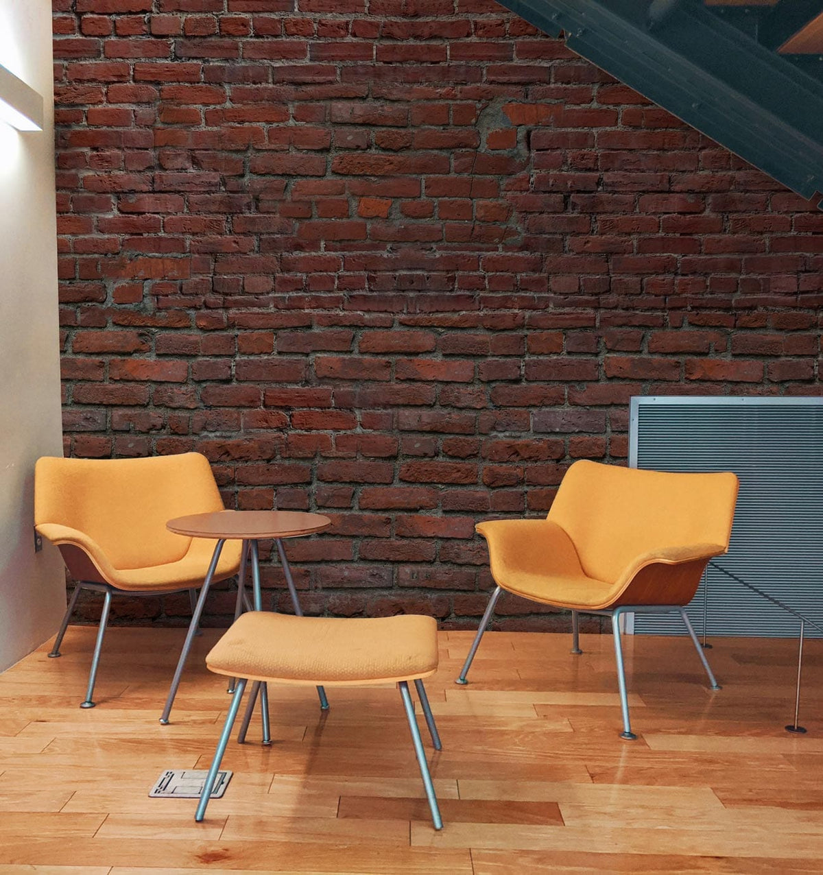 Rustic Red Brick Industrial Mural with orange chairs, wooden flooring, and metal accents in modern room.