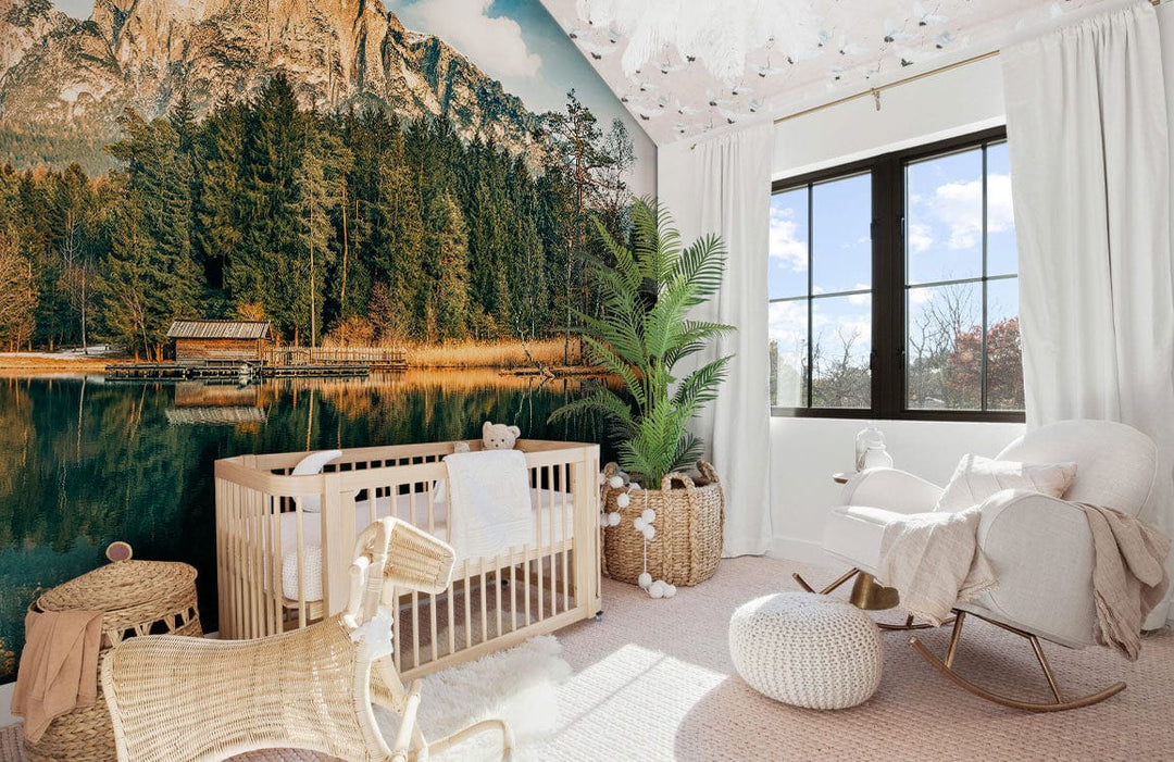 Baby room with serene mountain lake mural wallpaper, earthy tones, rattan crib, cream rocking chair.