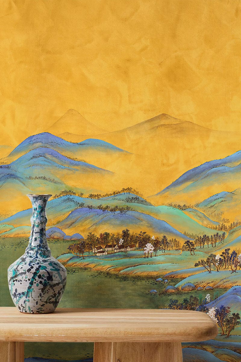 Golden Tranquility mural wallpaper with blue mountains behind wooden table and decorative vase.
