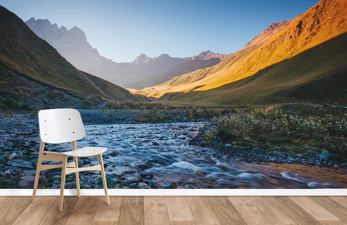 Sublime Mountain Valley Landscape Mural Wallpaper in warm tones, wooden flooring, white chair, scenic design.