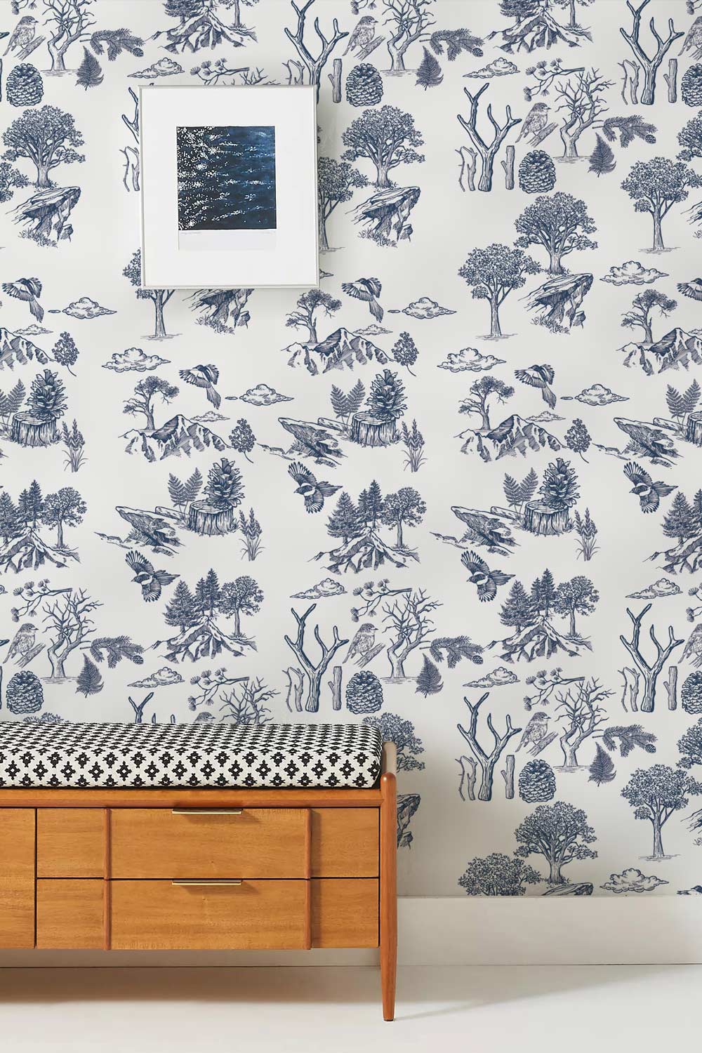 Navy and white forest wallpaper in living room with wooden bench, patterned cushion, framed artwork.