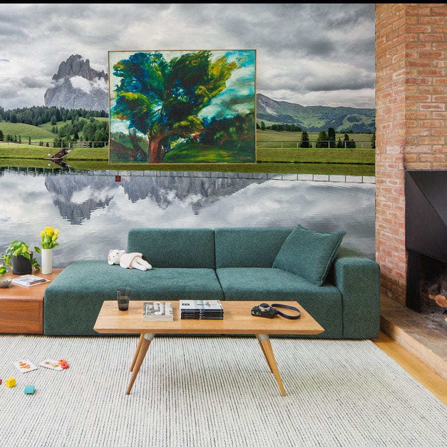 Green sofa, modern mural wallpaper, Serene Mountain Reflection; calming greens and greys, rustic brick fireplace.