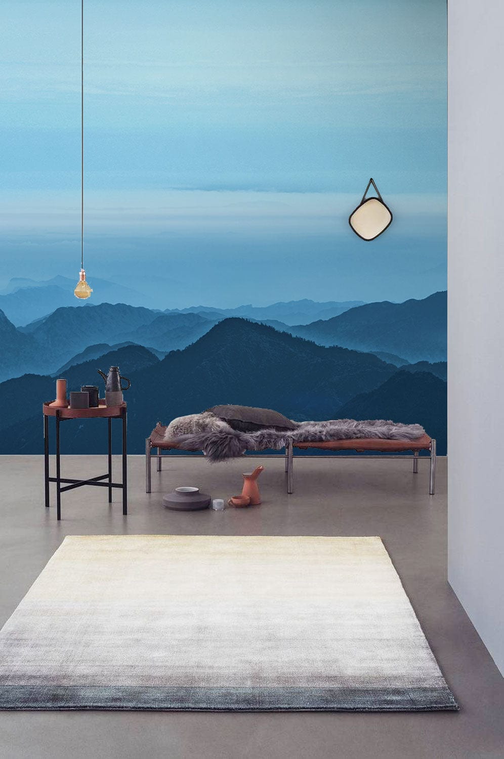 Tranquil blue mountain mural wallpaper in minimalist room with grey floor, modern bench, pendant light.