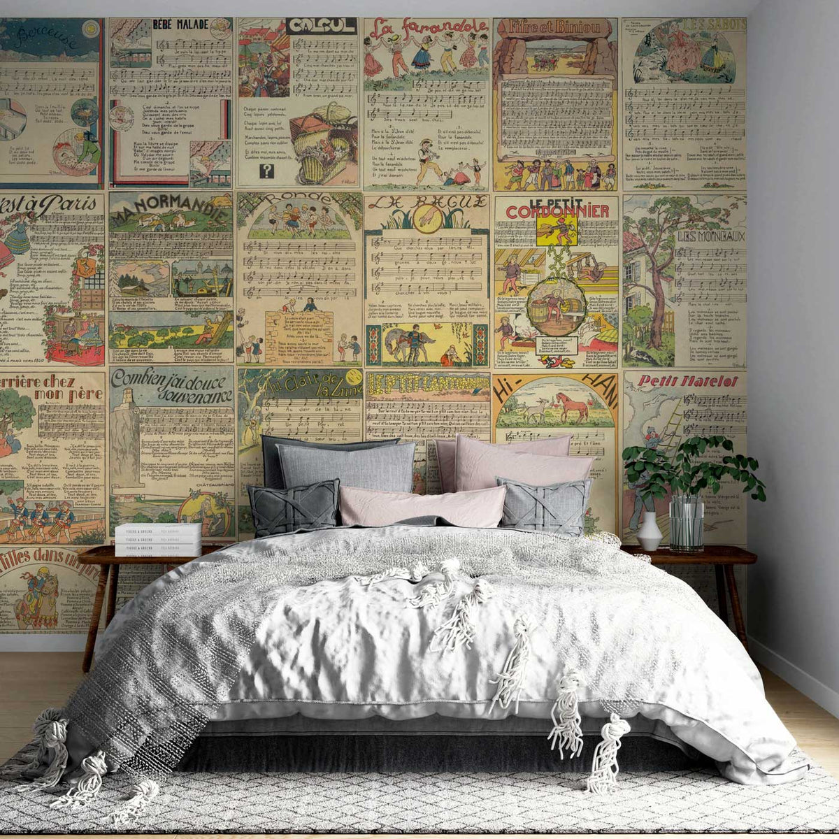 Vintage French newspaper-style collage wallpaper in bedroom with grey bed, wooden flooring, and white walls.
