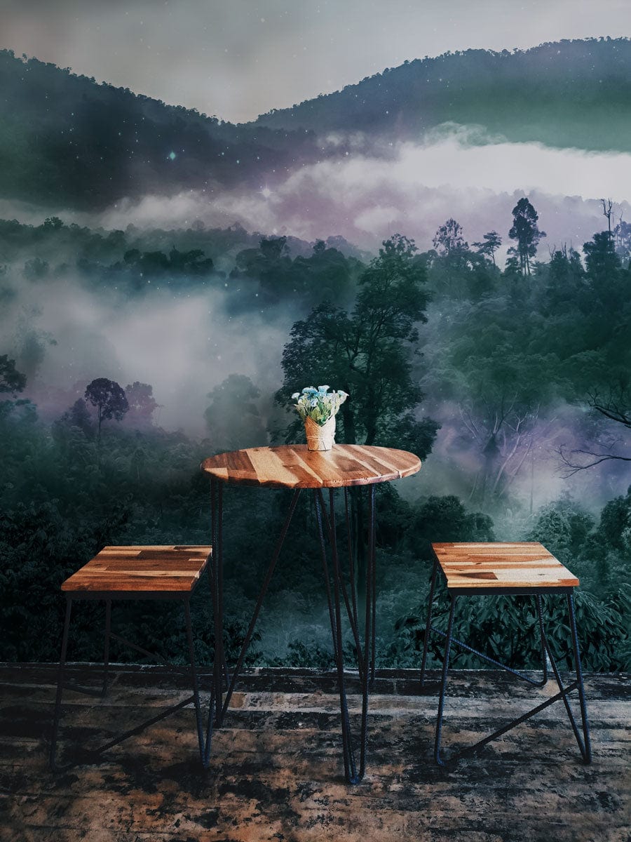 Mystical mural wallpaper in green hues, wood table and stools, industrial flooring, misty forest scene.
