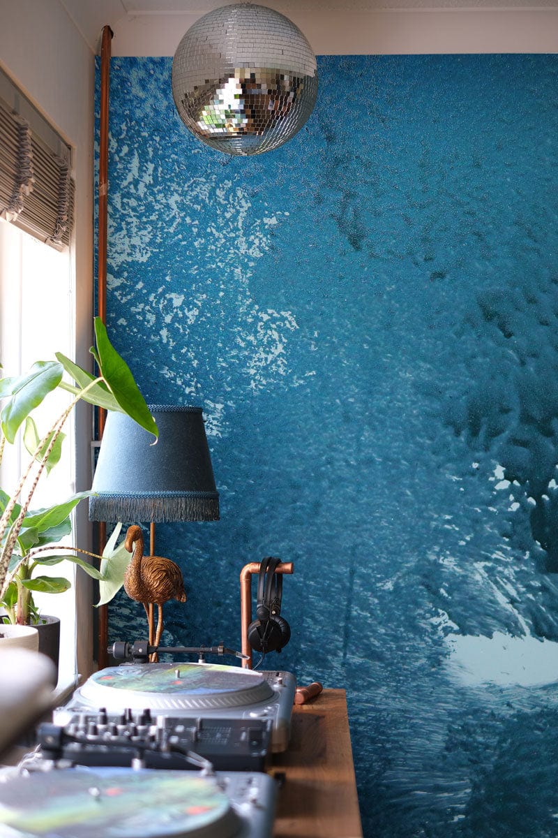 Teal ocean wave mural wallpaper in modern living room with disco ball and wood accents.