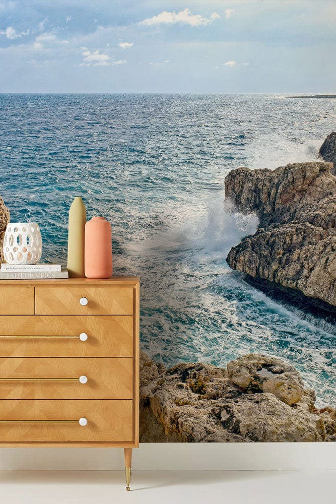 Coastal mural wallpaper with sea and rocks, natural wood chest, coastal cliff serenity theme.