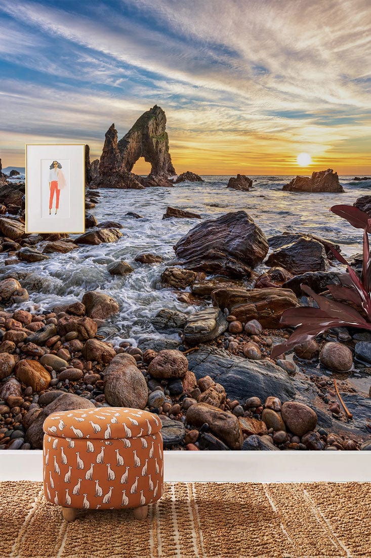 Sunset Coastal Landscape Mural, dramatic rocks, orange patterned pouffe, textured rug, living room decor.