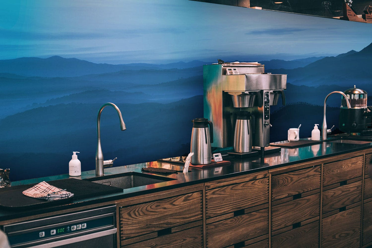 Wooden kitchen counter against Tranquil Blue Misty Mountains Mural Wallpaper, featuring stainless steel appliances.
