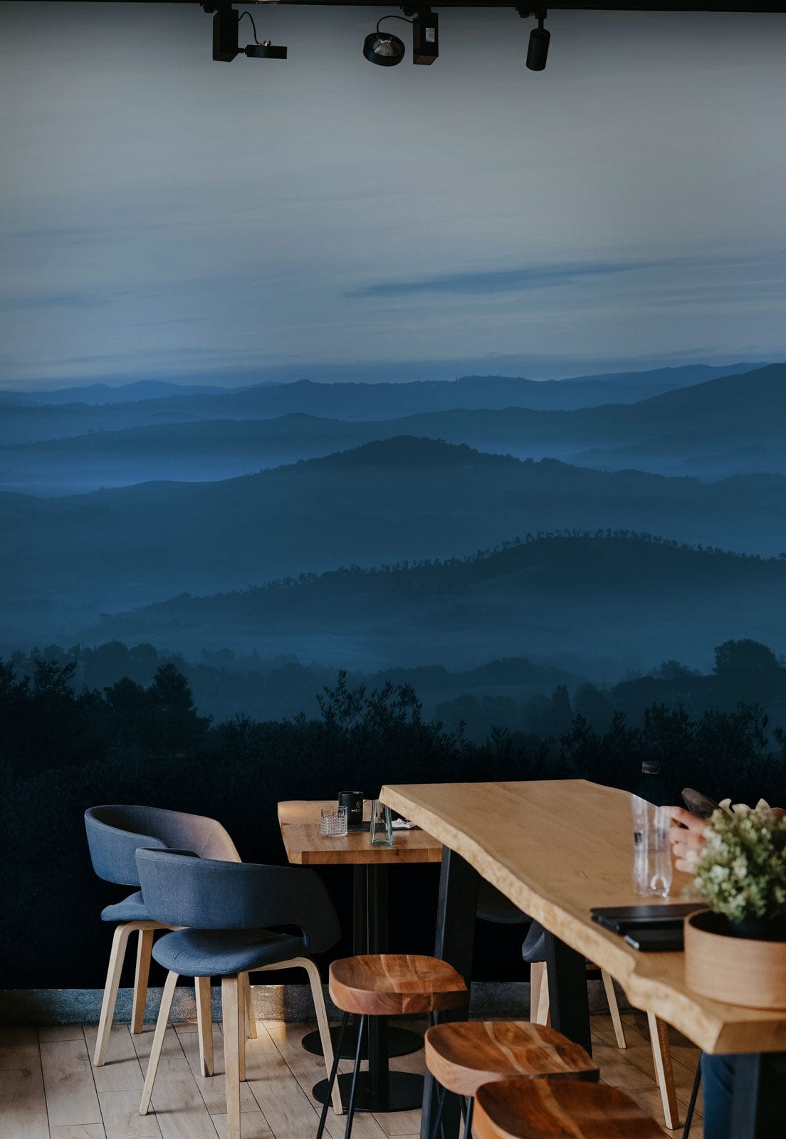 Tranquil Blue Misty Mountains Mural Wallpaper with modern chairs and wooden dining table in restaurant.