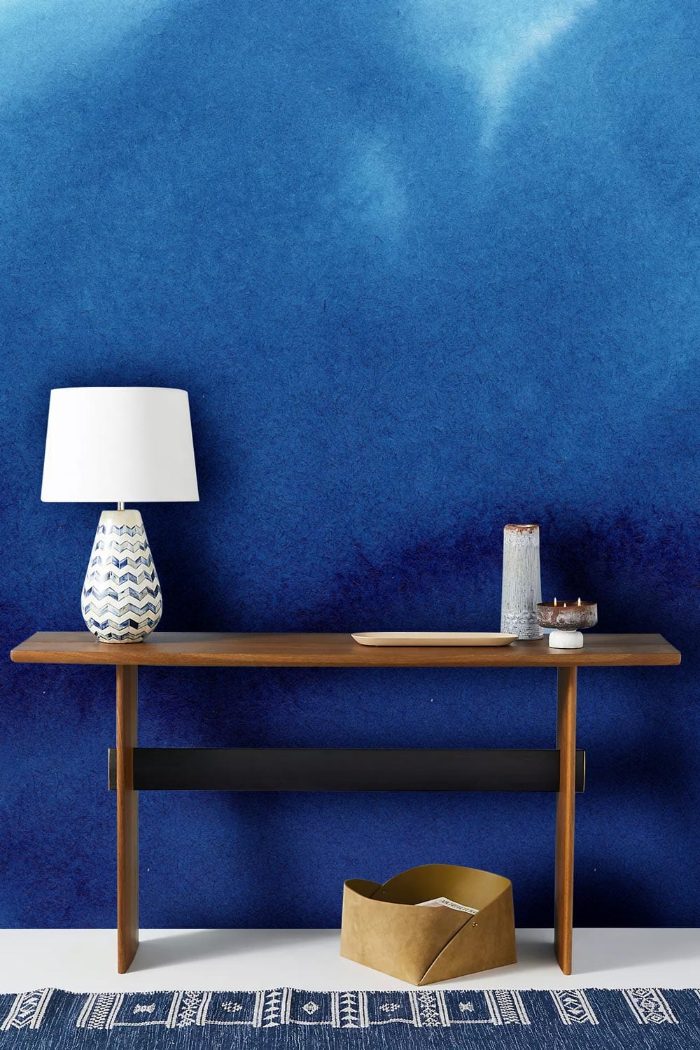 Deep Blue Watercolour Wash Accent Wallpaper, wooden console table, geometric lamp, tribal pattern rug.