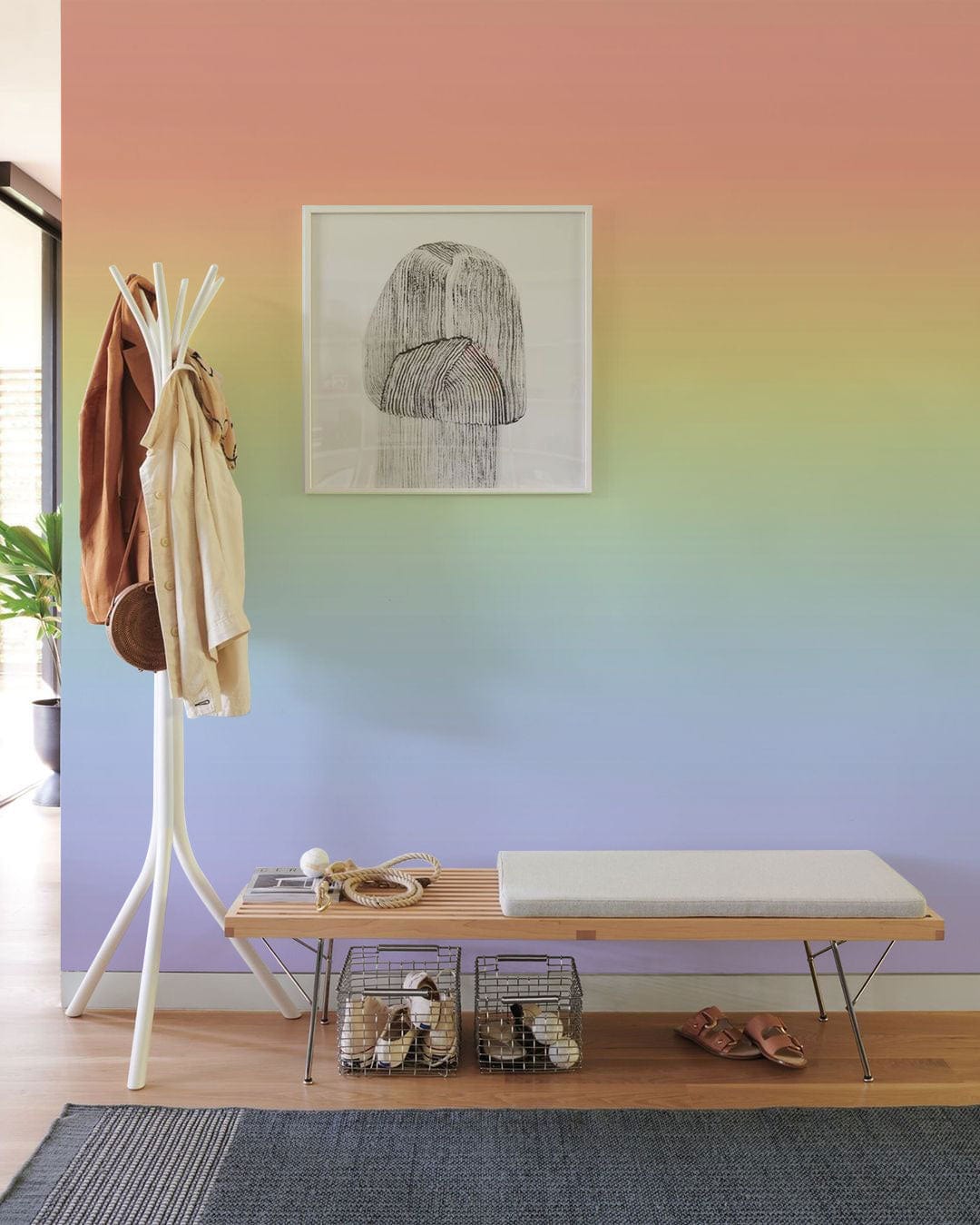 Pastel rainbow gradient wallpaper in modern interior entryway with bench, coat rack, and artwork.