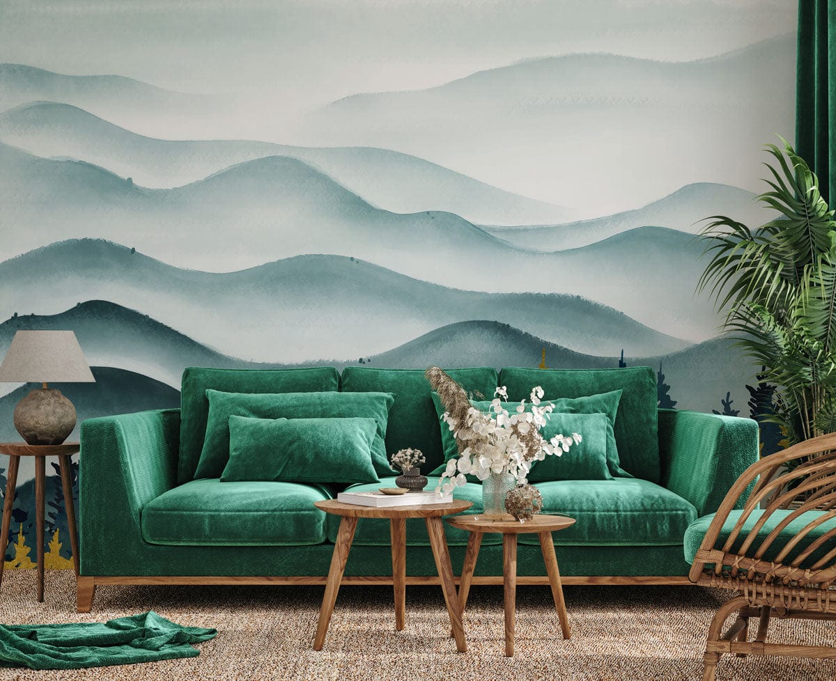 Tranquil Blue Forest mural wallpaper in living room with green velvet sofa, wicker chair, wooden tables.