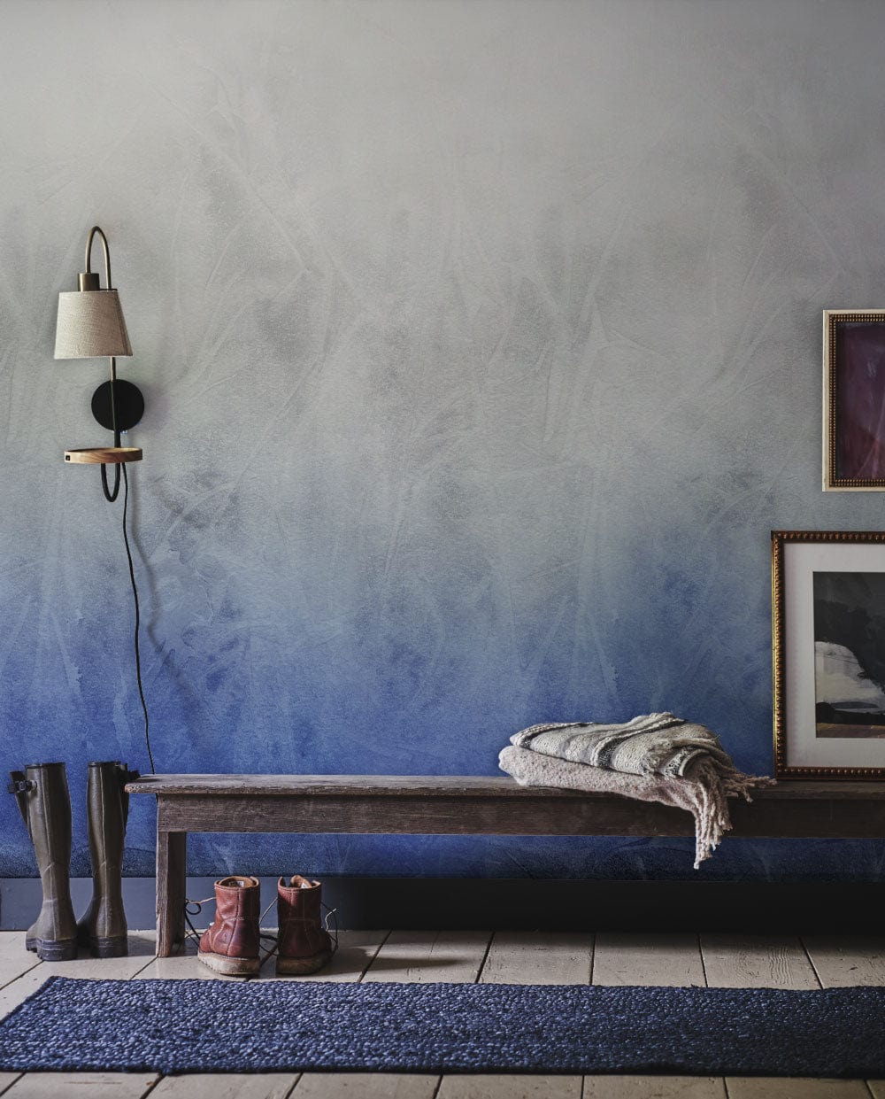 Ethereal Misty Blue Gradient Mural Wallpaper in living room with wooden bench, blue rug, and lamp.