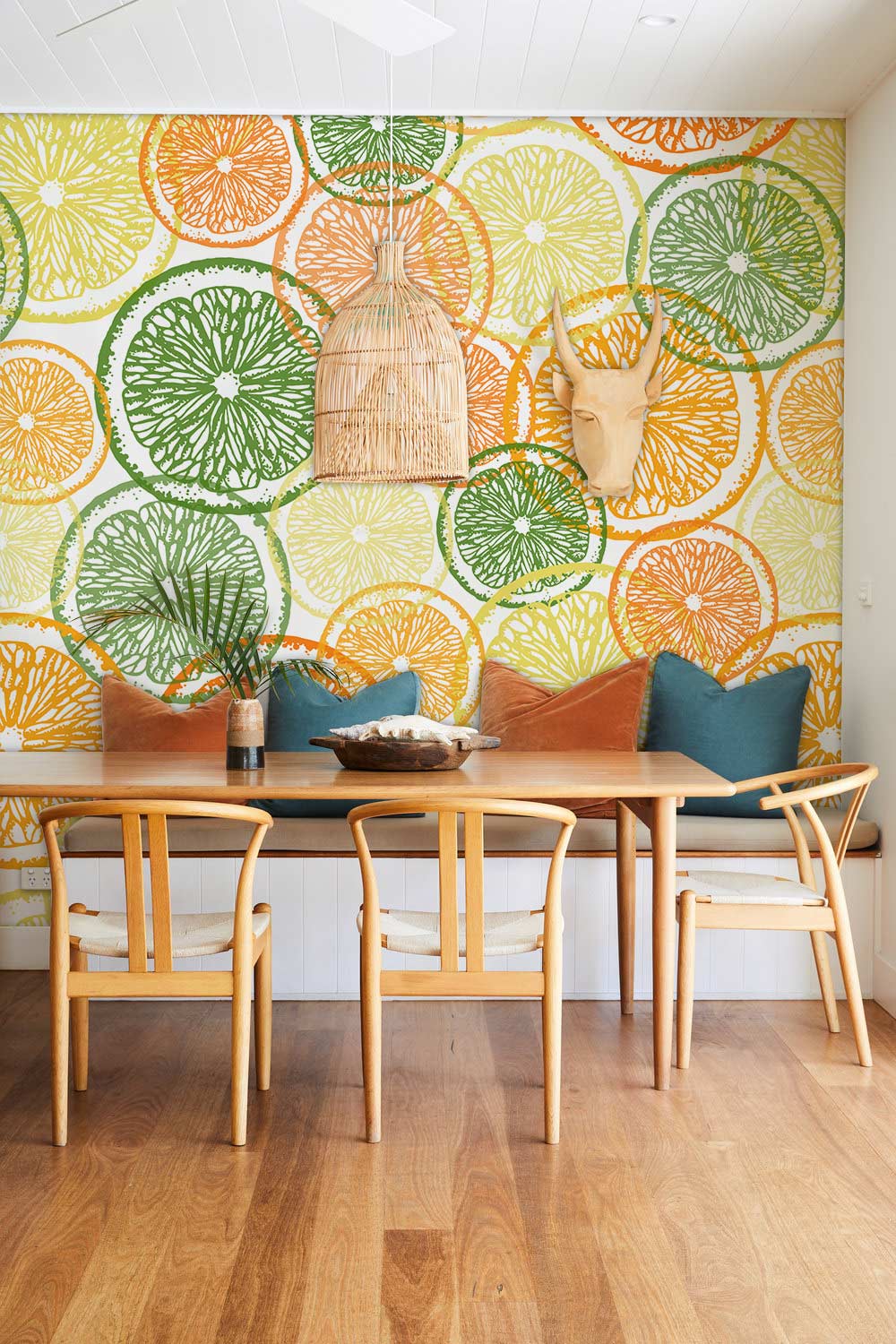 Dining room with citrus fruit slice wallpaper, wooden table and chairs, pendant light, and wooden flooring.