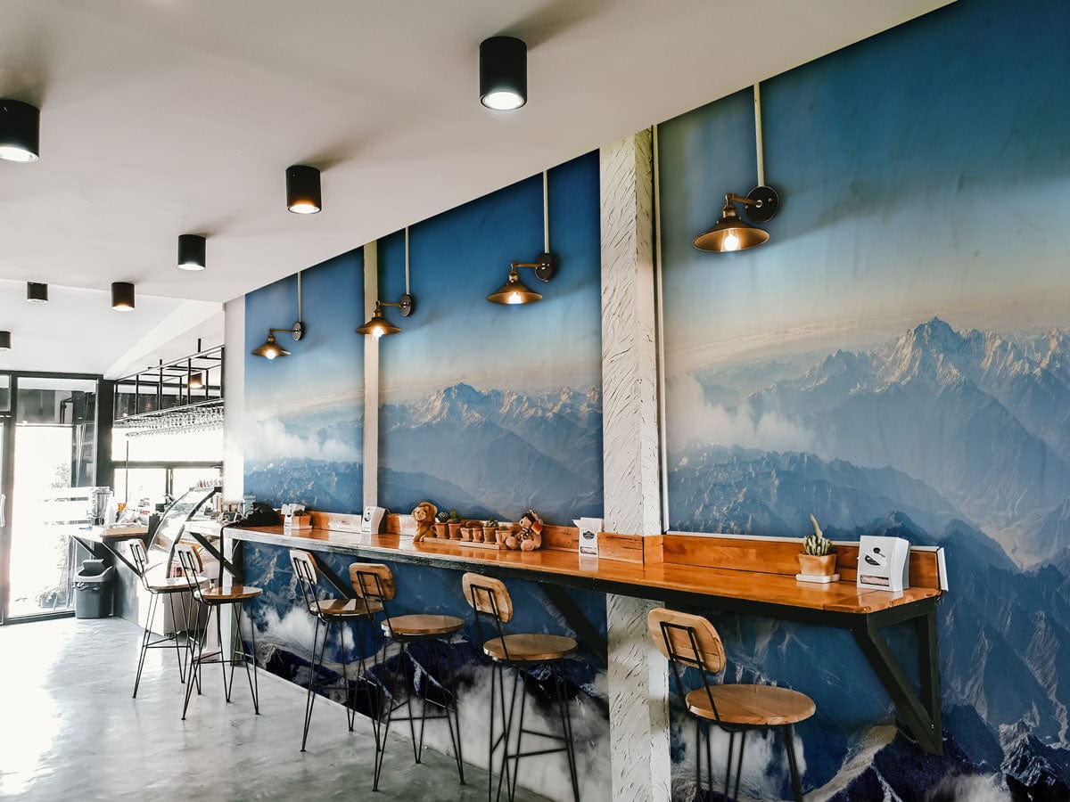 Panoramic Mountain Vista Mural Wallpaper in cafe with wooden countertops, metal stools, and panel lighting.
