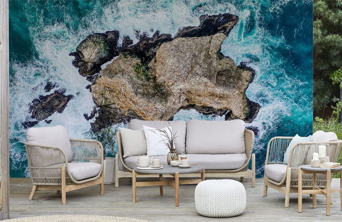 Aerial Coastal Rockscape mural in oceanic hues, wicker furniture, neutral tones, wooden flooring, outdoor setting.