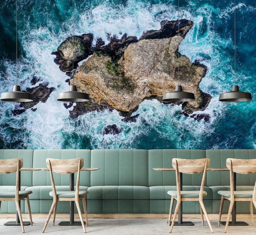 Aerial Coastal Rockscape Mural Wallpaper with wooden chairs, teal sofa, industrial lighting in dining area.