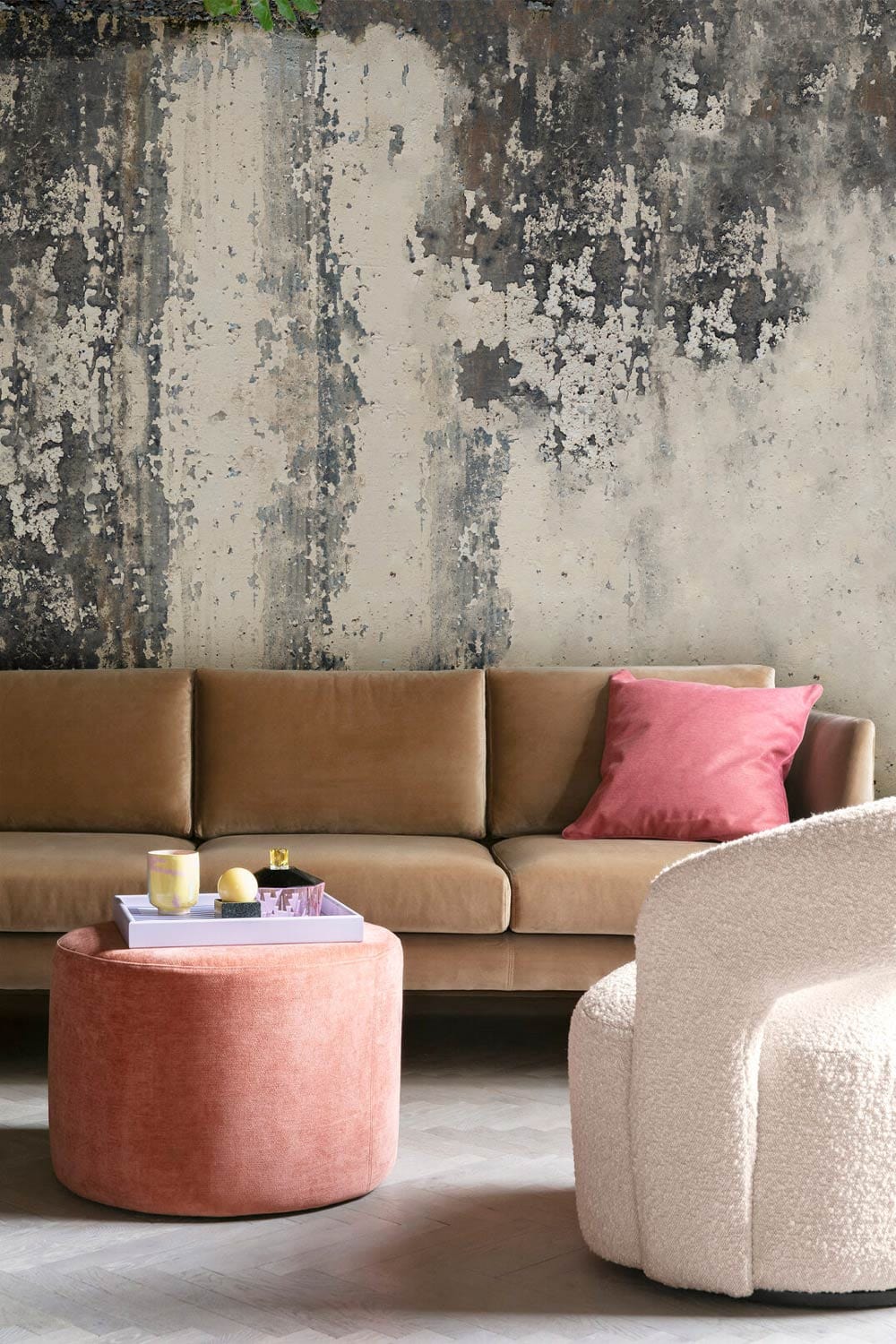 Vintage-inspired grunge mural with brown sofa, pink cushion, plush chair, and rustic grey wall.