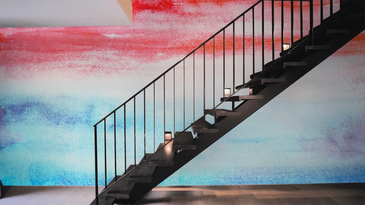 Vibrant sunset watercolour mural wallpaper behind modern black staircase, grey flooring, colourful wall art.