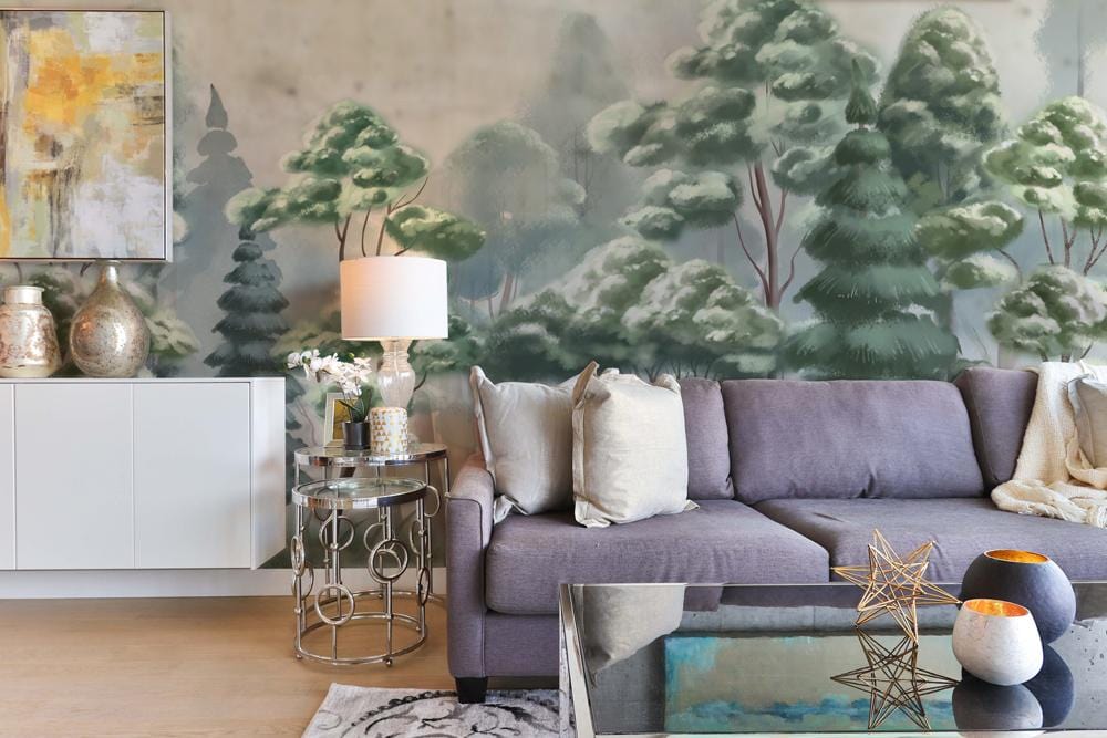 Green watercolour trees mural wallpaper with grey sofa, glass table, white sideboard, and abstract artwork.