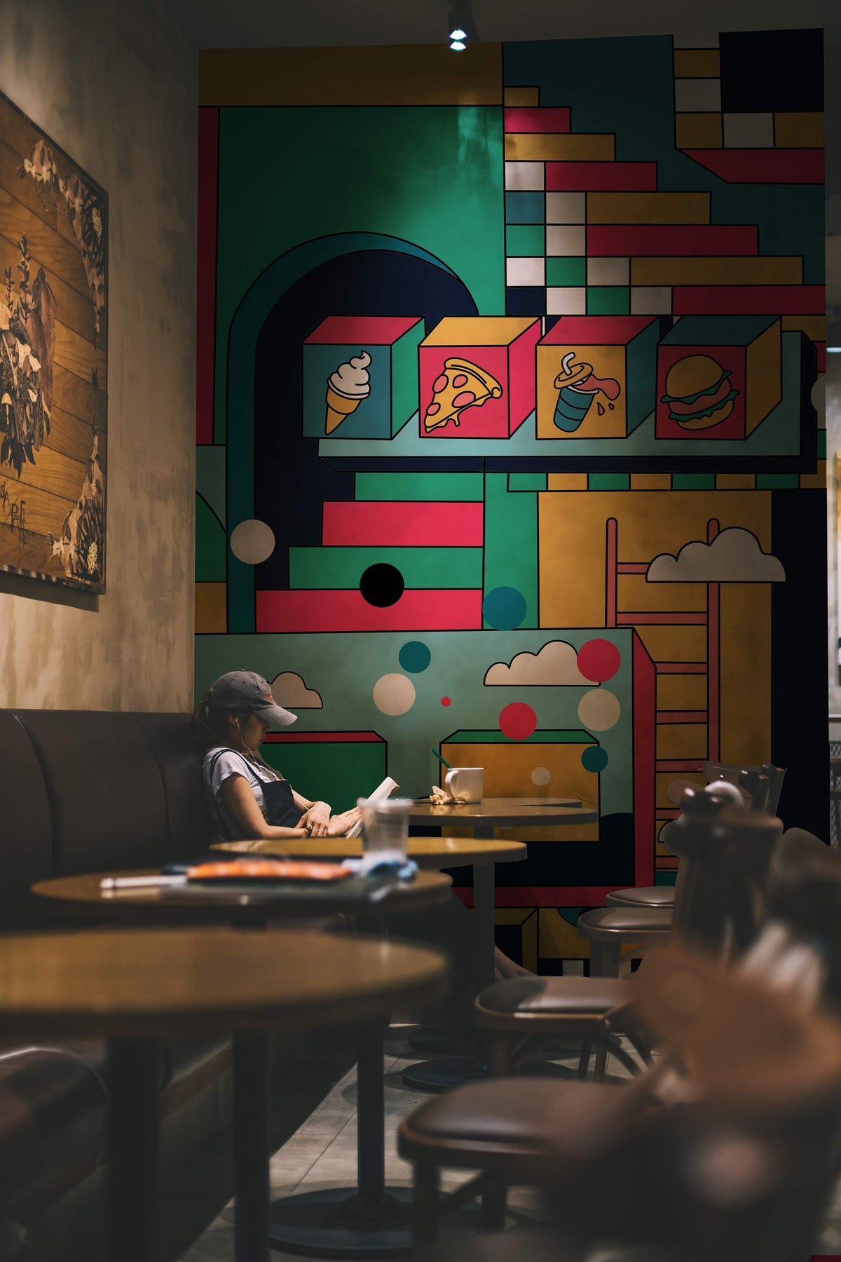 Retro Geometric Abstract Wallpaper in café; bold multicolour art complements modern leather seating, wooden tables.