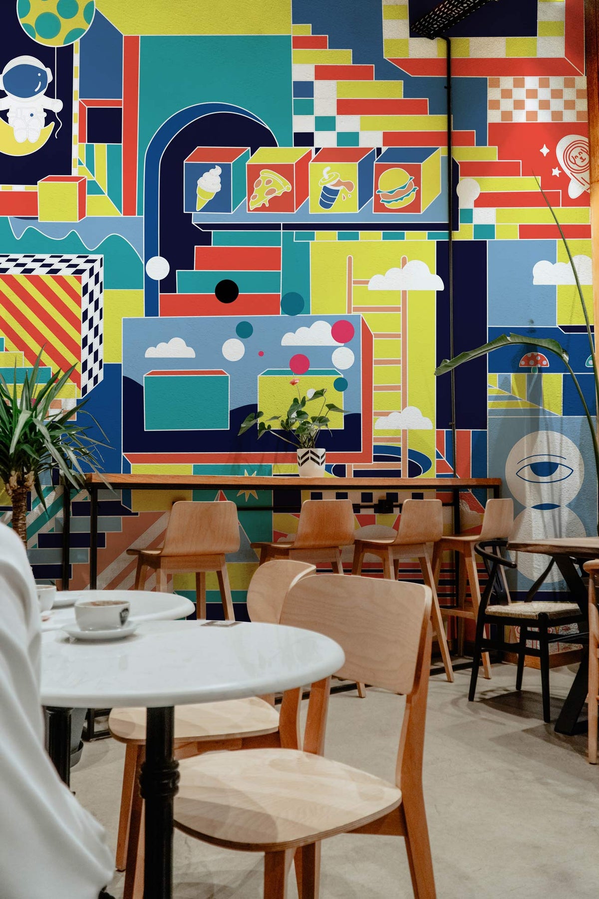 Retro Futuristic Geometric Multicolour Space Adventure Mural Wallpaper in vibrant café setting with wooden furniture.