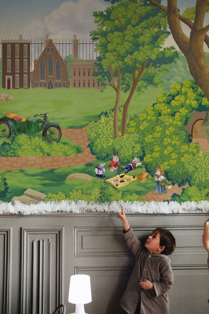 Vintage countryside picnic wallpaper mural; grey panelling; child pointing; vibrant greenery; indoor setting.