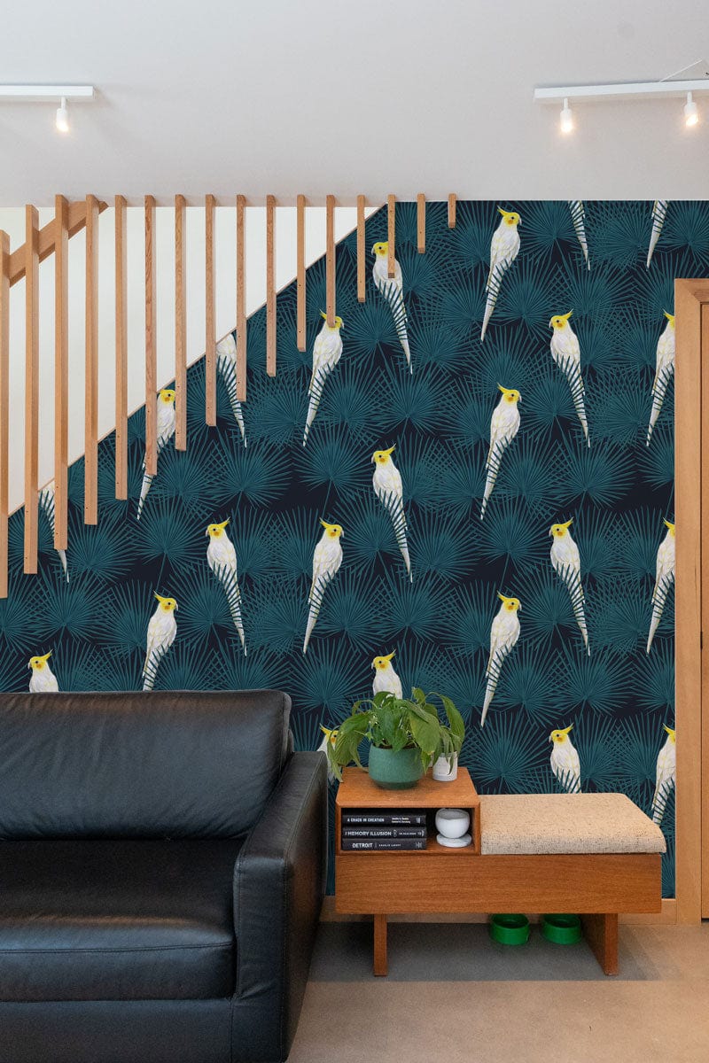 Tropical cockatoo wallpaper in teal, black leather sofa, light wooden accents, modern living room design.