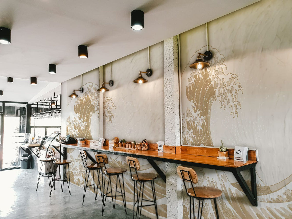 Beige Japanese Wave Mural Wallpaper in café with wooden bar stools and industrial lighting decor.