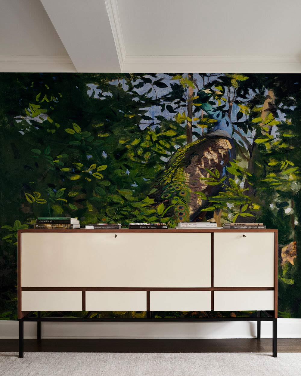 Peacock mural wallpaper with green nature theme behind mid-century modern console in a living room.